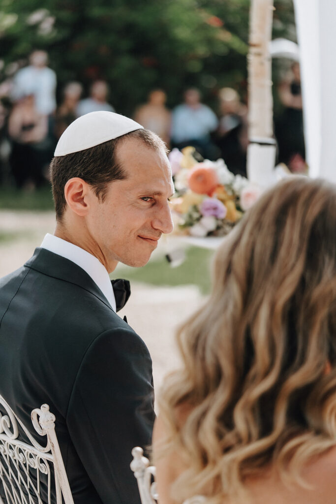 Groom-looking-at-bride-during-ceremony-under-white-houppa-romantic-and-emotional-moment-wedding-in-provence-chateau-de-robernier-sea-bride-and-sun